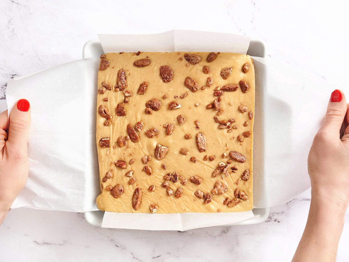 Hands removing homemade pumpkin spice fudge from a baking dish.