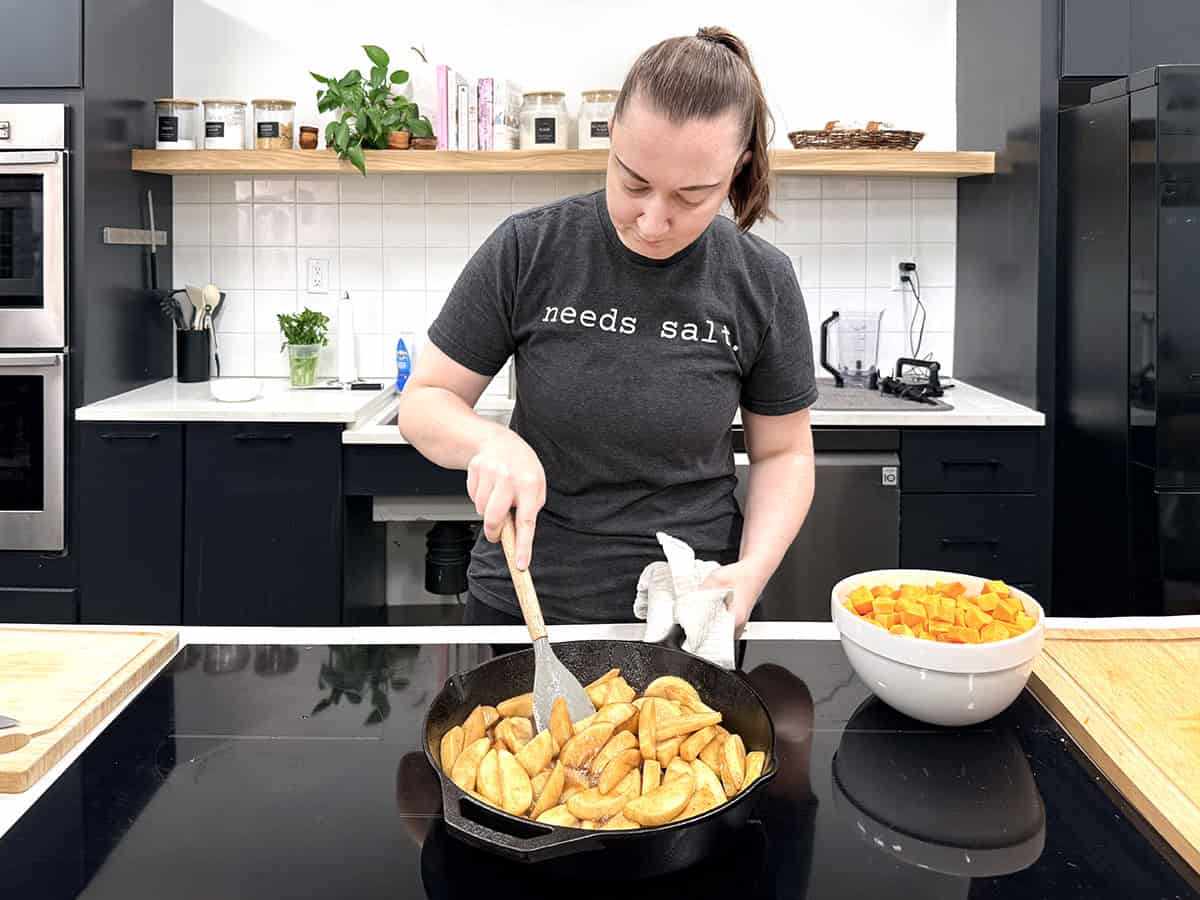 A woman cooking fried apples on a stovetop in a kitchen.