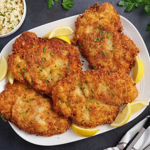 Overhead view of four chicken schnitzels on a plate.