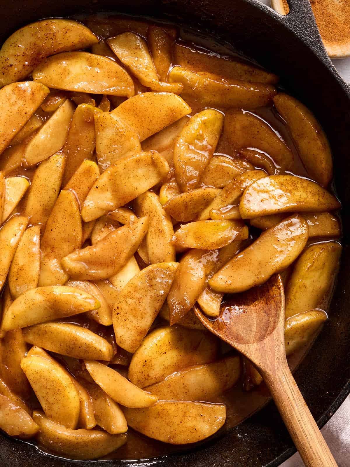 Overhead view of a skillet of fried apples with a wooden spoon stirring them.