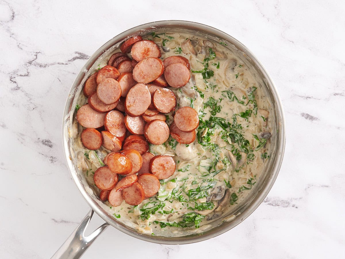 Browned sliced turkey sausage added to a creamy kale and mushroom sauce in a skillet.