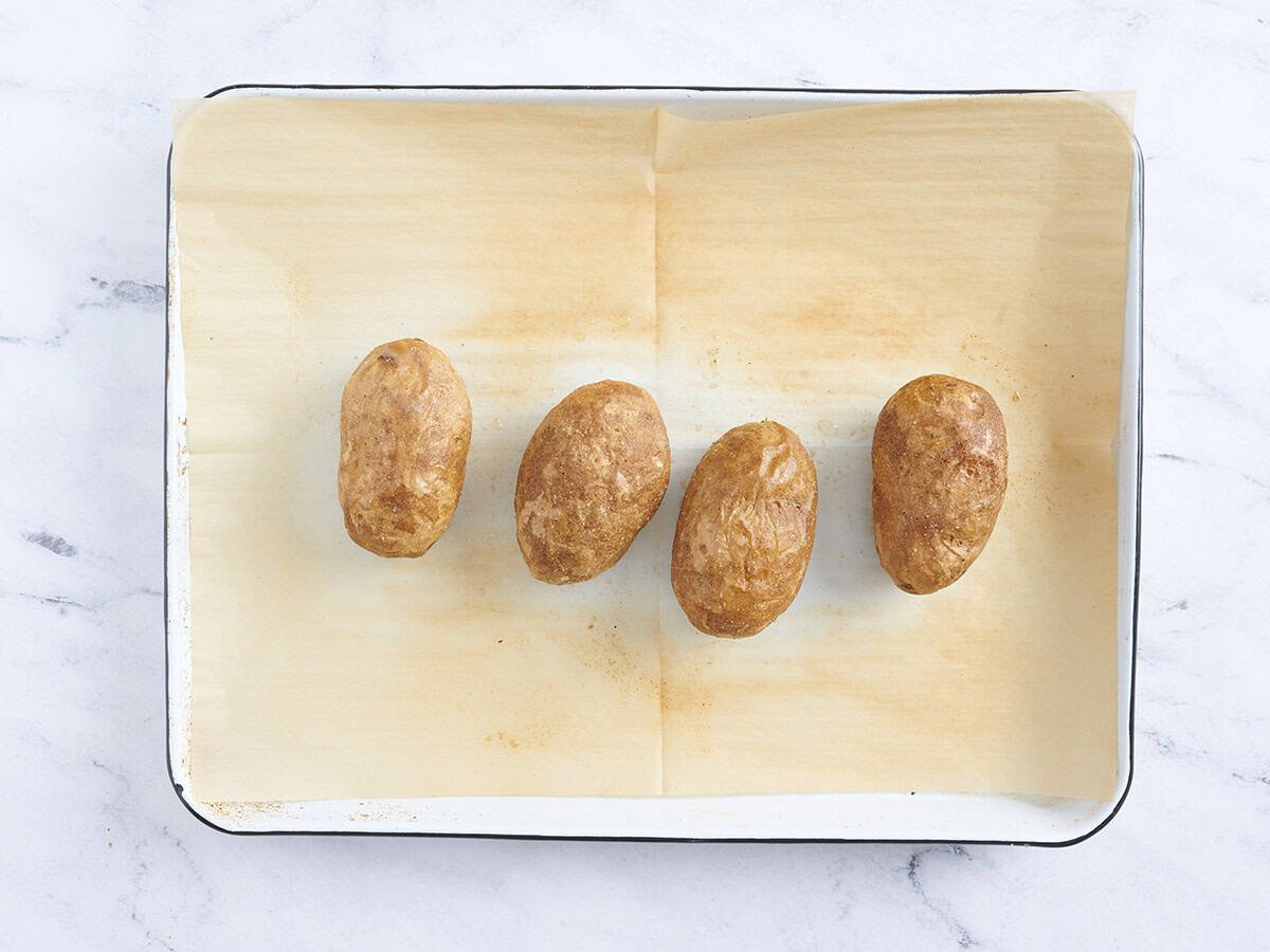 Four baked potatoes on a baking sheet.