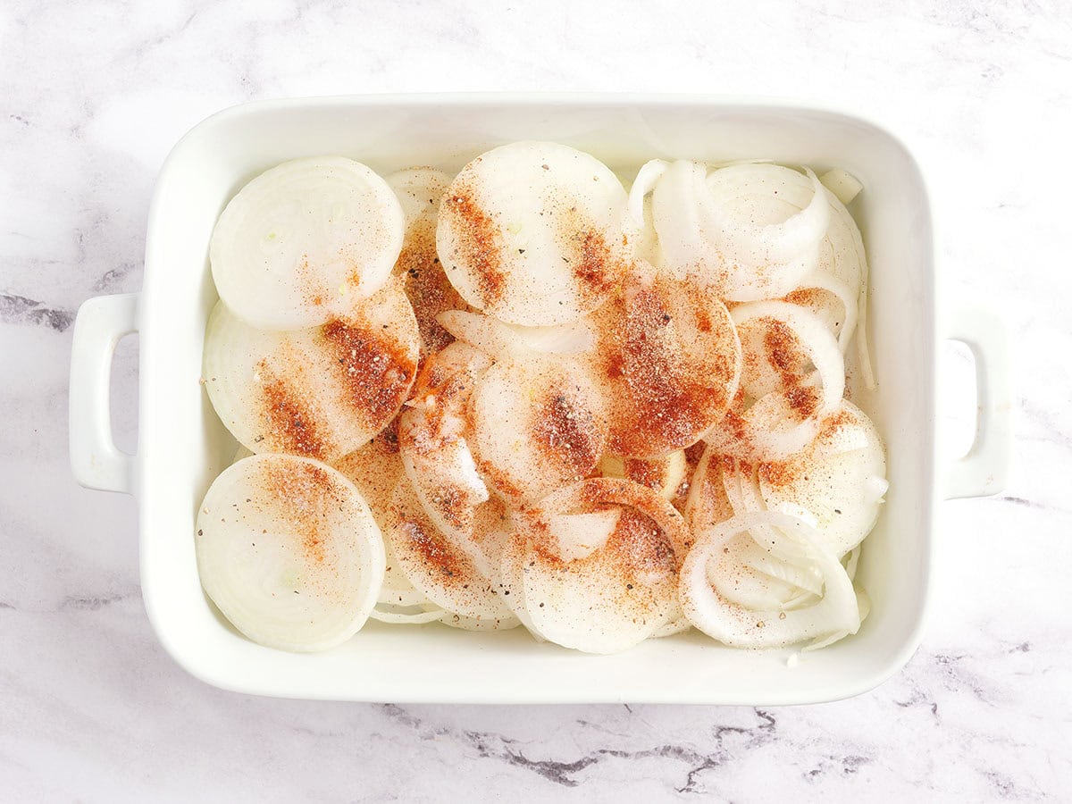 Sliced sweet onions with seasonings in a baking dish.
