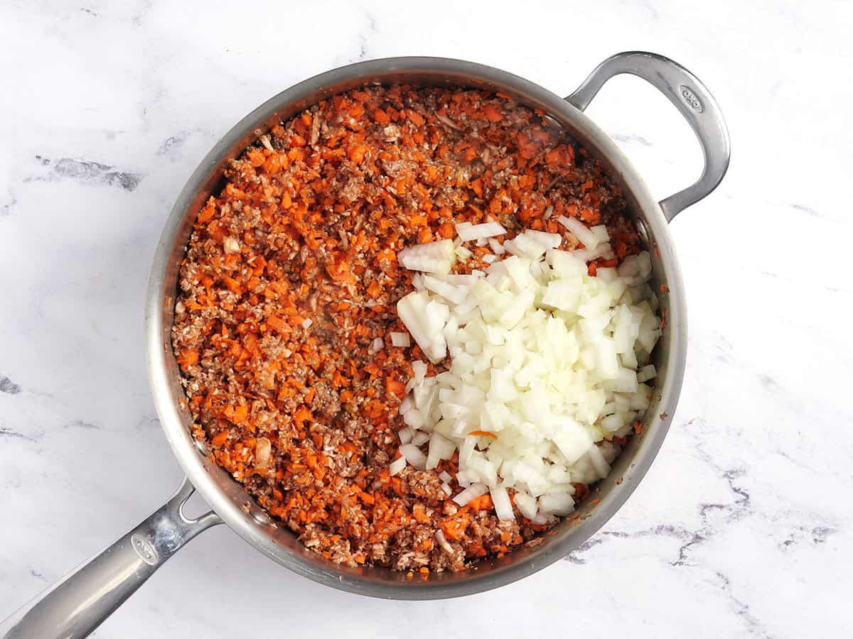 Processed carrots, mushrooms and onion in a sauce pan.