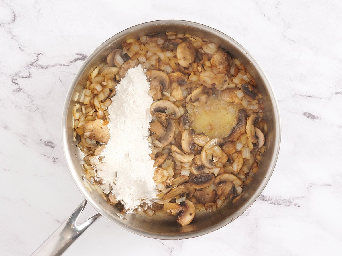 Flour added to sauteed mushrooms and onions in a skillet.