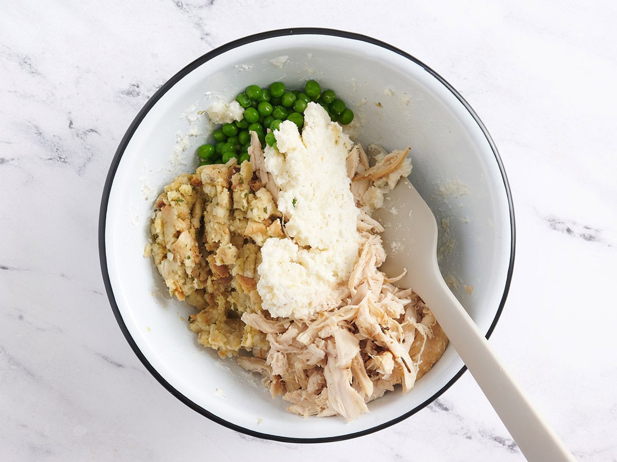 Peas, stuffing, and turkey meat added to a bowl with potato skin filling.