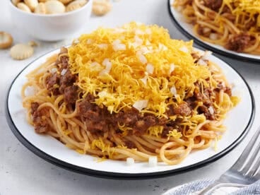 Side view of a plate of Cincinnati chili with shredded cheese and diced onions.
