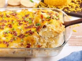 Side view of a twice baked potato casserole with a spoon taking some out the dish.