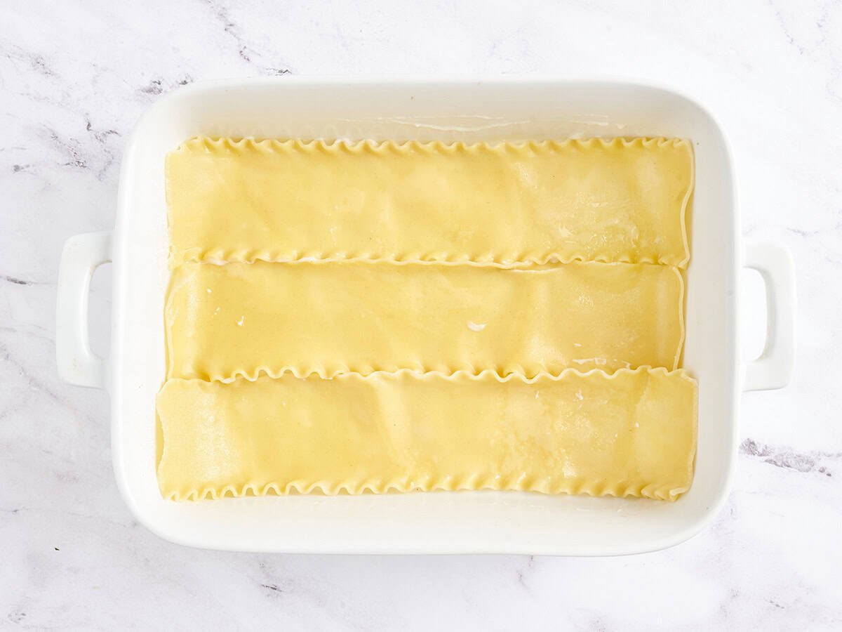 Cooked lasagna noodles added to a baking dish.