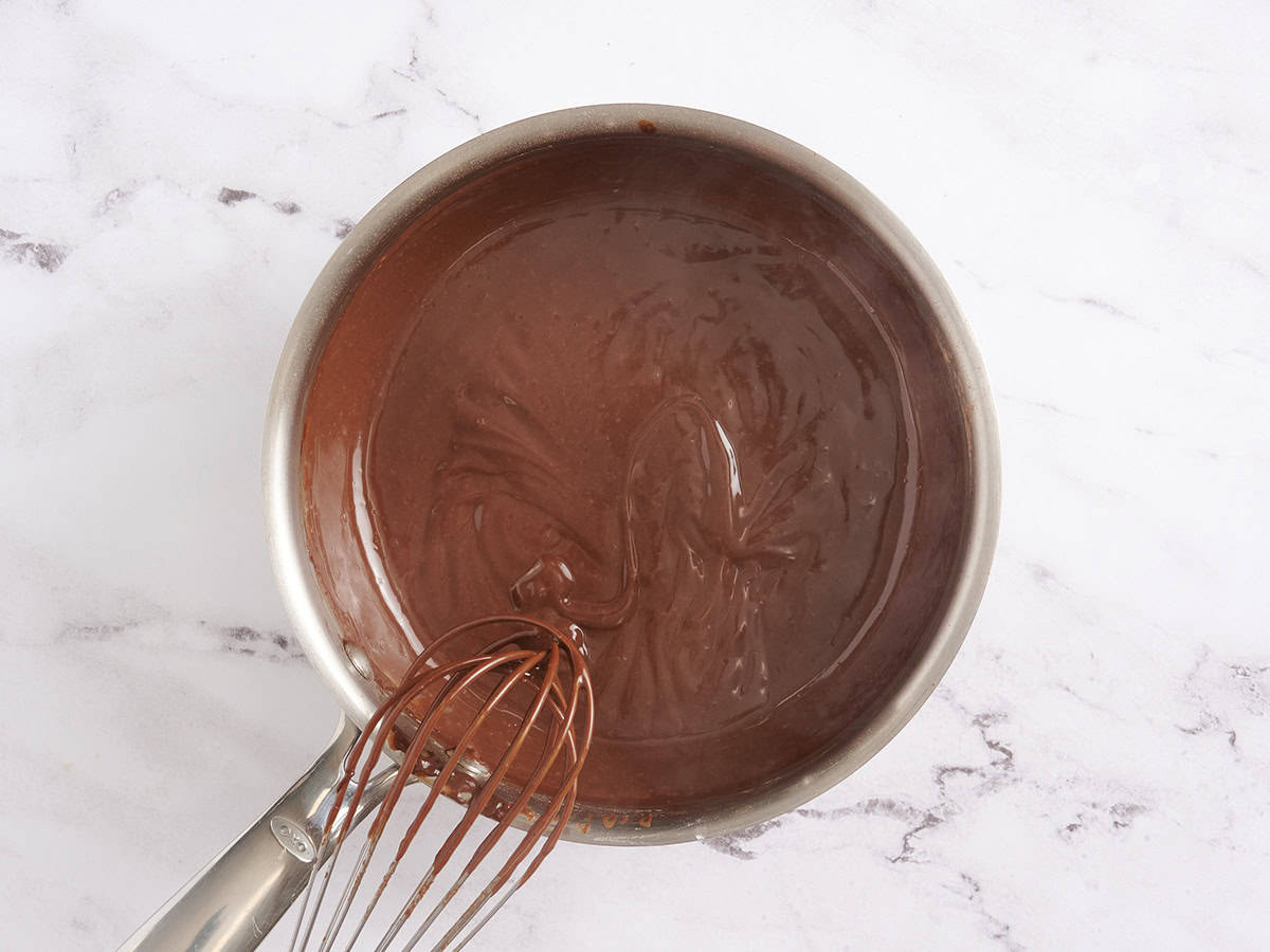 Chocolate pudding in a saucepan with a whisk.