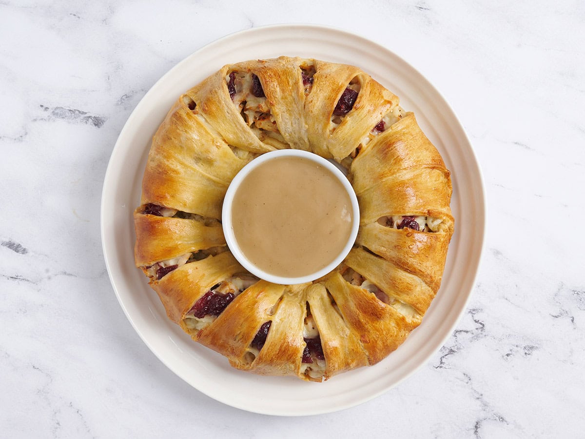 Baked holiday wreath with a bowl of gravy in the middle.