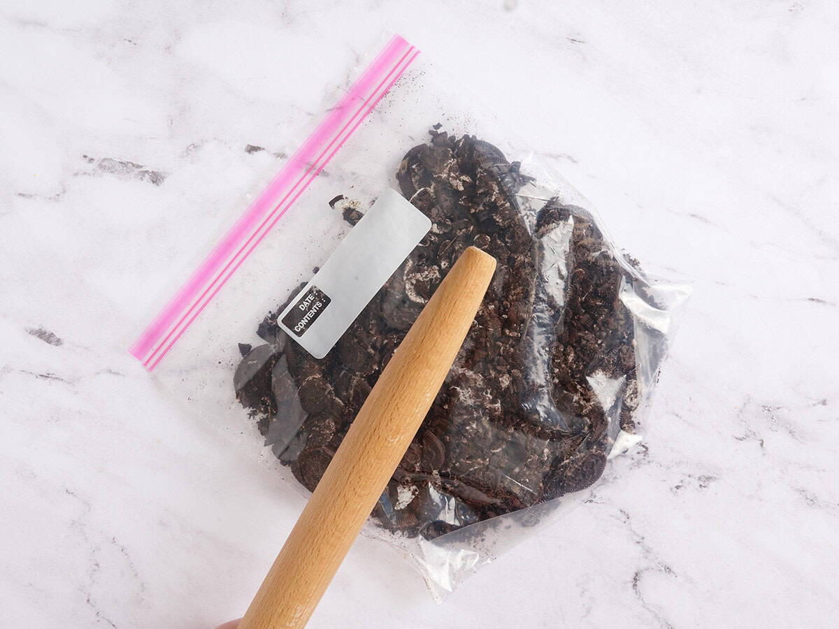 A rolling pin crushing chocolate sandwich cookies in a ziplock bag.