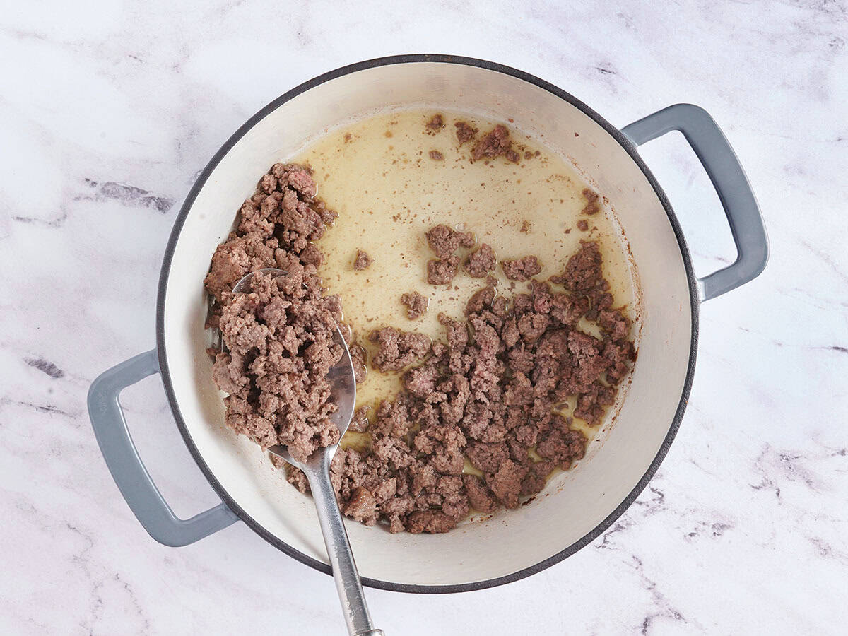 A spoon removing browned ground beef from a pot.