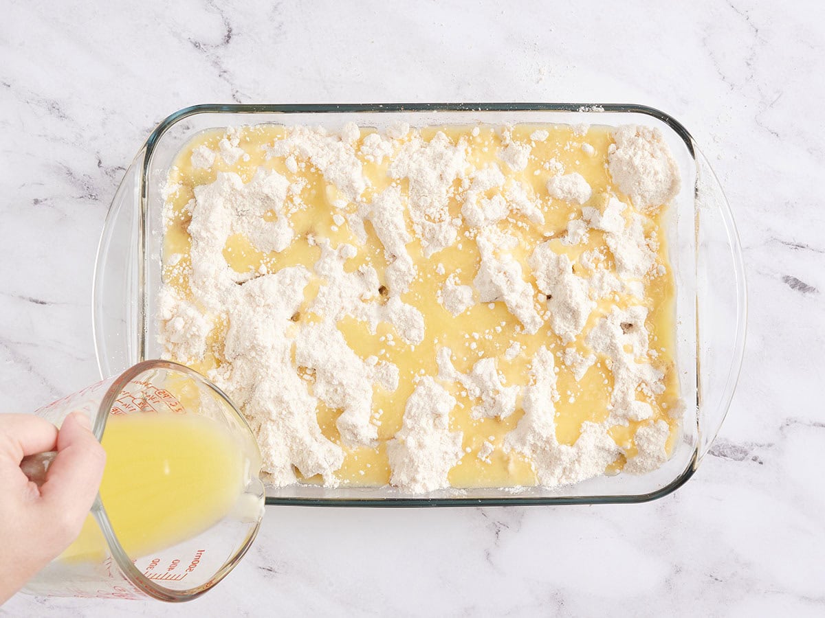 Melted butter being poured over the ingredients for an apple dump cake in a baking dish.