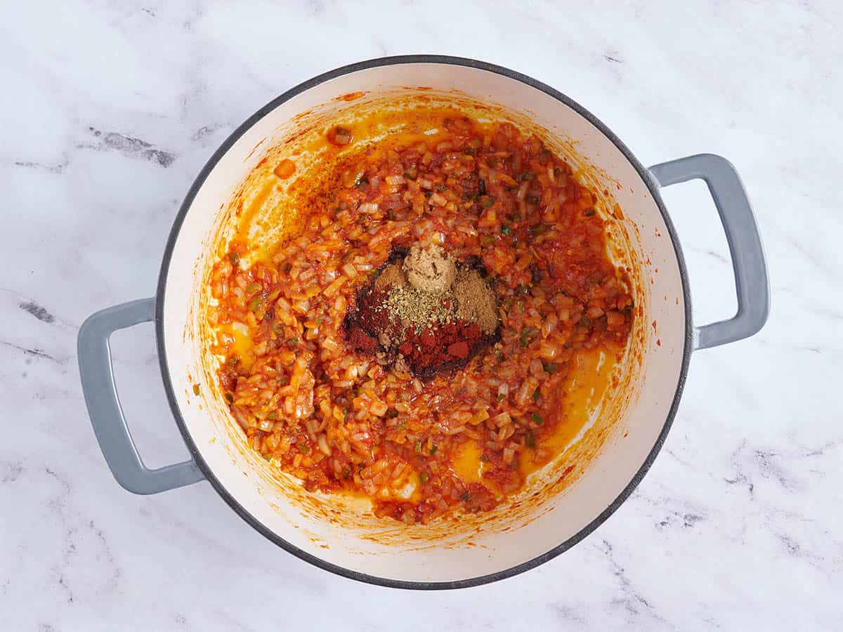 Seasonings added to tomato paste and onions in a pot to make Texas chili.