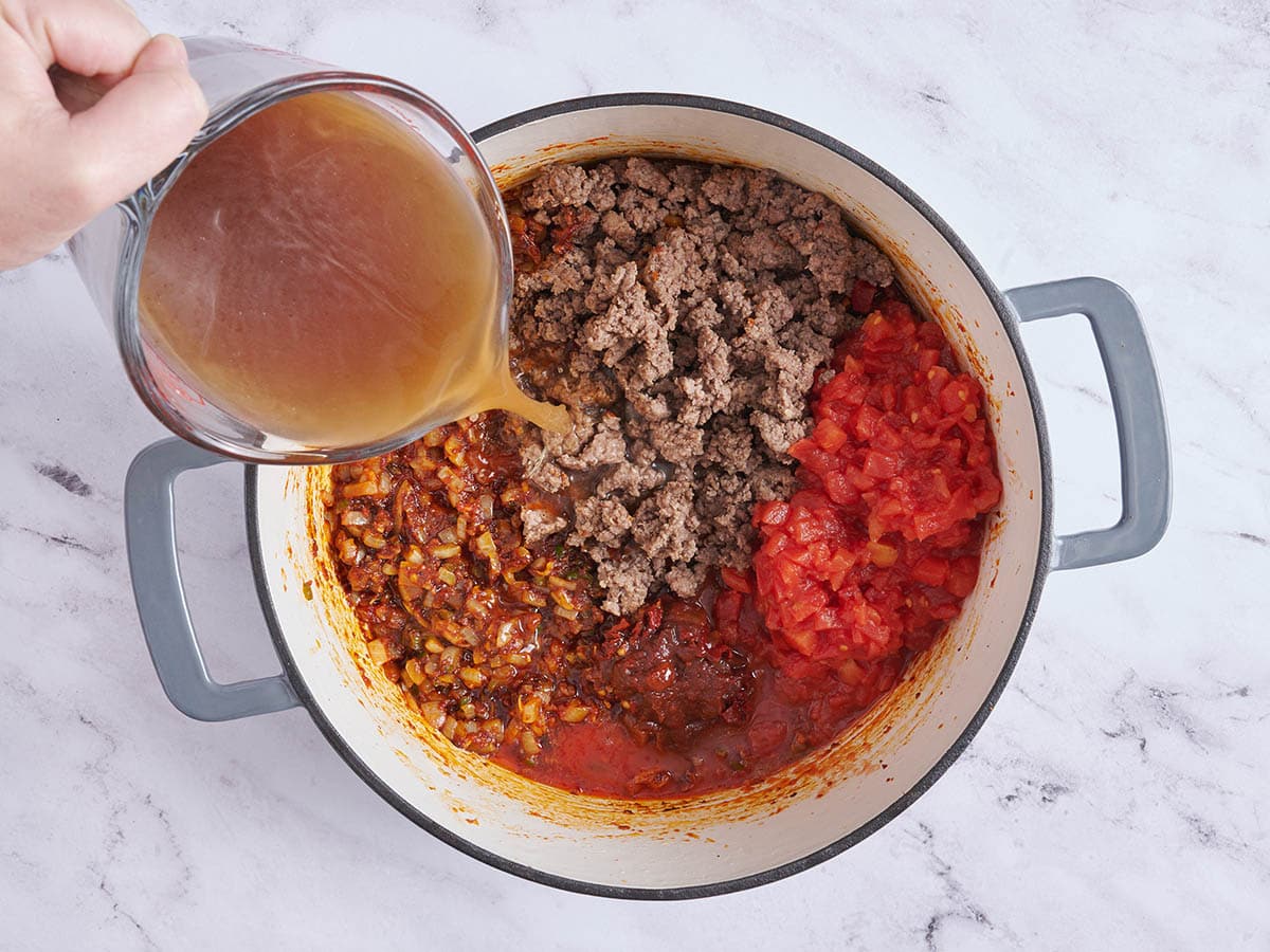 Diced tomatoes, browned ground beef and beef stock added to a pot of sauteed onions.