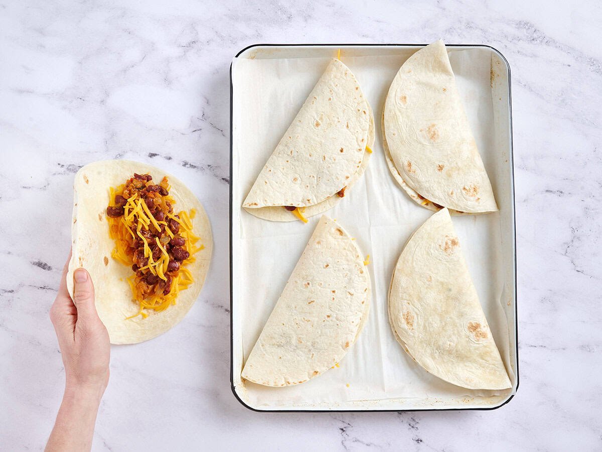 A hand folding a quesadilla next to a baking sheet of other quesdillas.