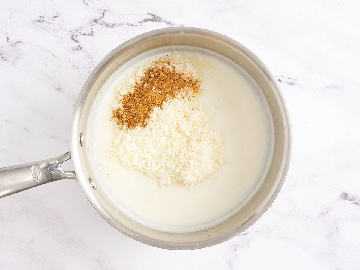 Parmesan and seasonings in a white cream sauce in a saucepan.