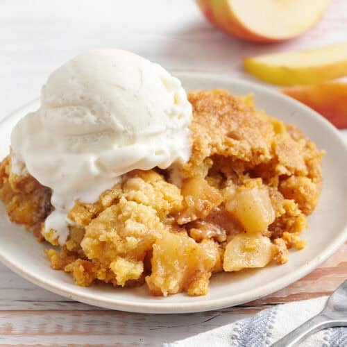 Side view of apple dump cake on a plate with a scoop of vanilla ice cream.
