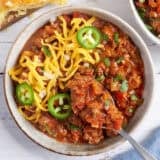 Overhead view of a bowl of Texas chili topped with shredded cheese and jalapeno slices with a spoon taking some.