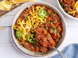 Overhead view of a bowl of Texas chili topped with shredded cheese and jalapeno slices with a spoon taking some.