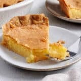 Side view of a slice of homemade chess pie on a plate with a fork taking some.