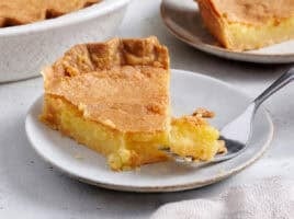 Side view of a slice of homemade chess pie on a plate with a fork taking some.