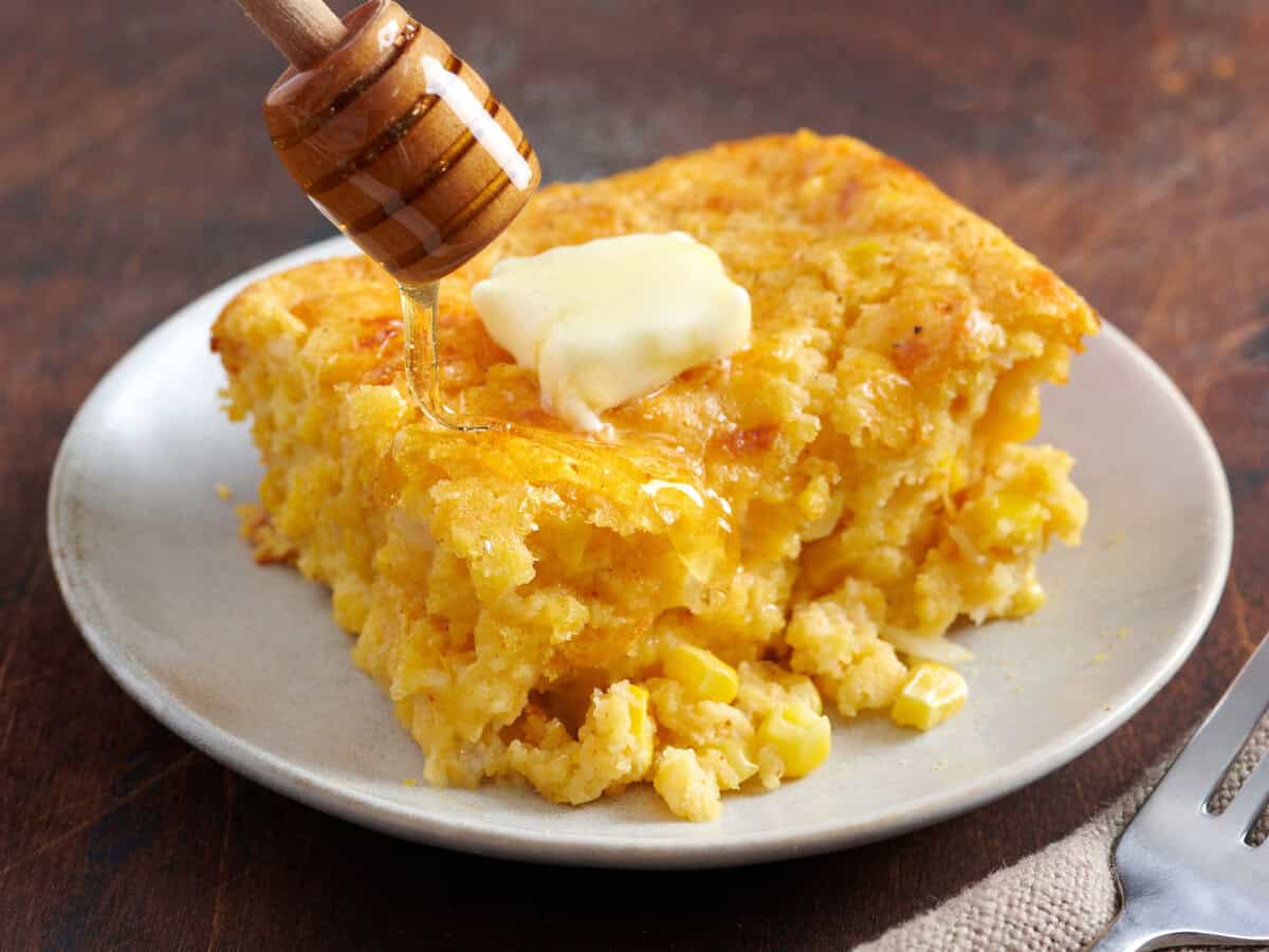 Cornbread casserole on a plate with a dollop of melting butter and honey drizzled on top.