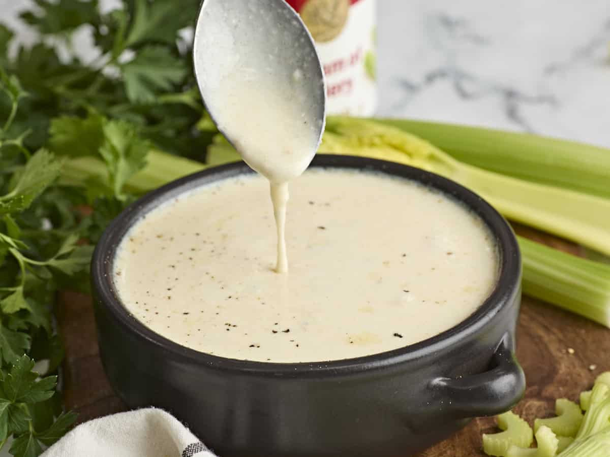 Side view of cream of celery soup in a bowl with a spoon being removed from the bowl.