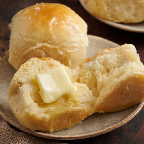 Hawaiian rolls on a plate. one with a pat of melting butter.