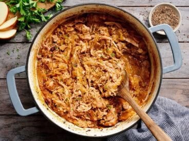 Overhead view of shredded pork and sauerkraut in a pot with a wooden spoon.