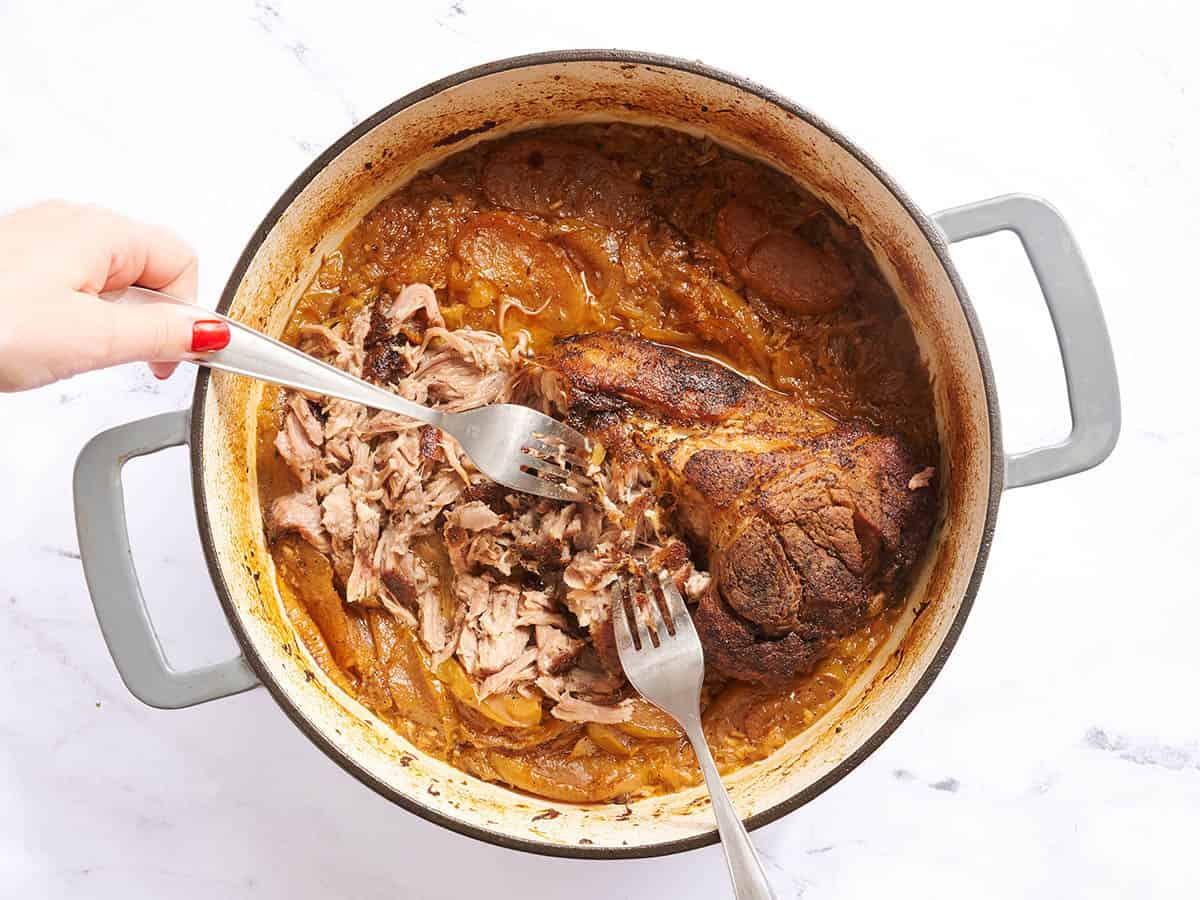 Forks shredding a pork butt in a dutch oven.