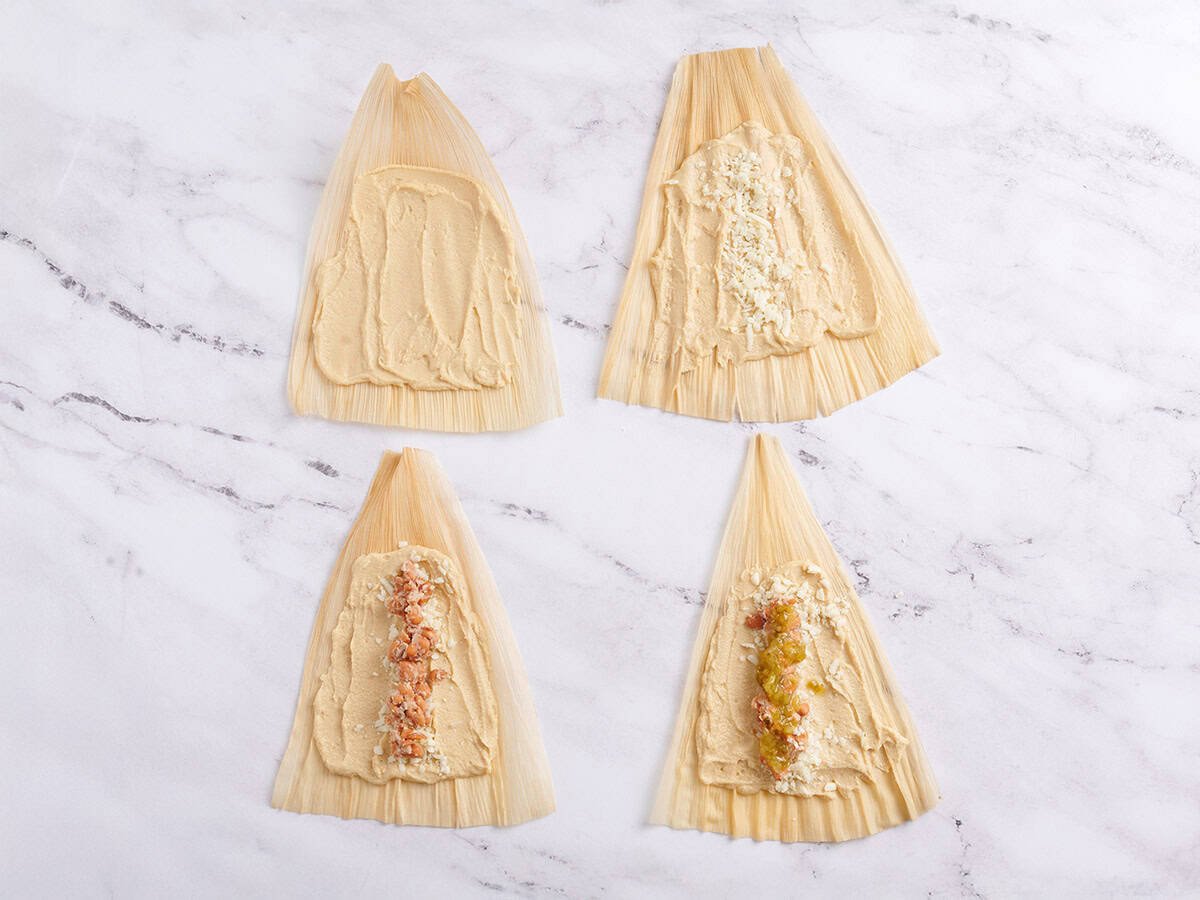 Corn husks being filled with tamale mixture.