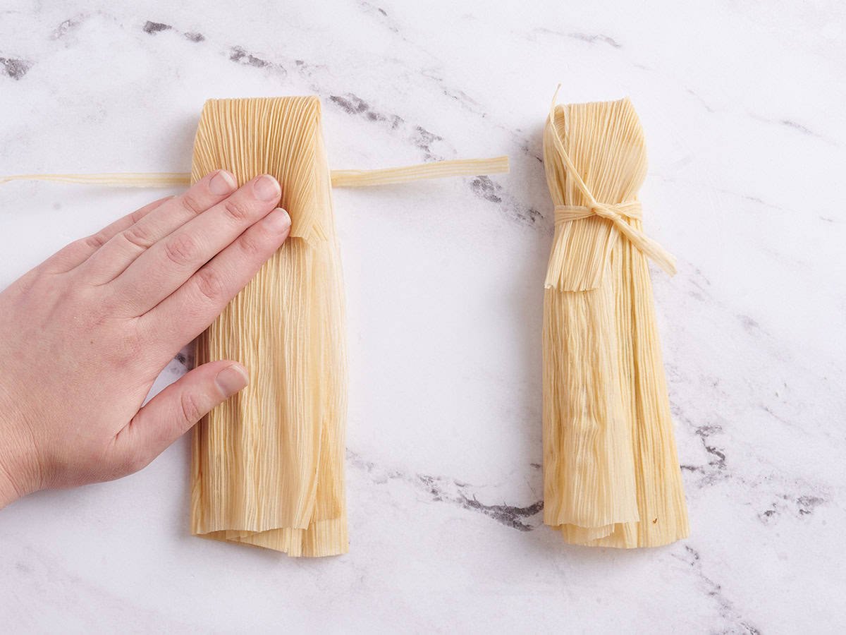 Hands folding a tamale.