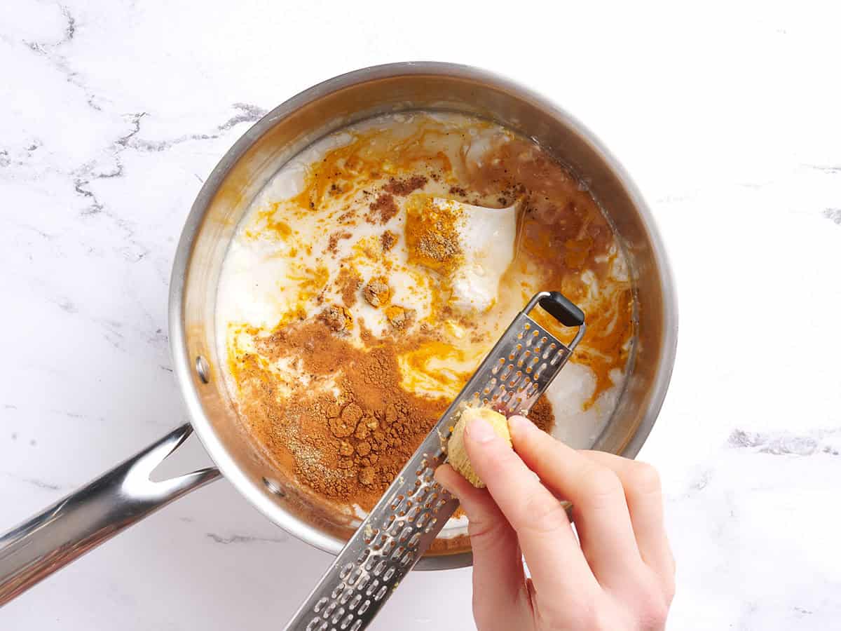 Grating ginger into the pot of ingredients to make golden milk.