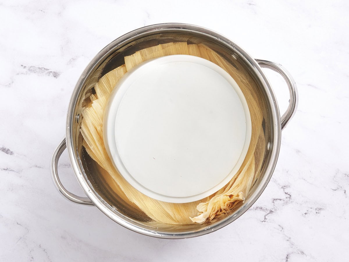 Corn husked weighed down in a saucepan.