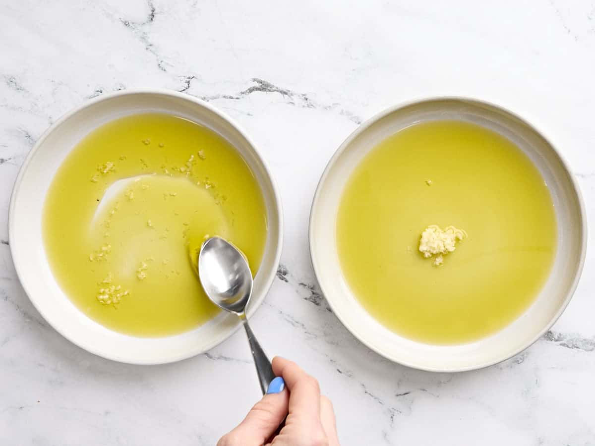 Olive oil and minced garlic in two white bowls with a spoon.