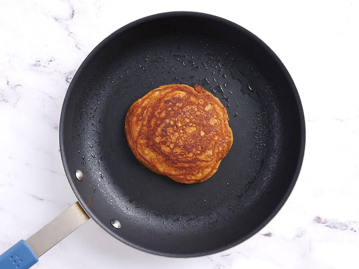 A gingerbread pancake cooking in a skillet.