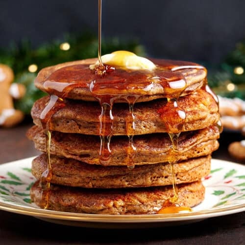Side view of a stack of gingerbread pancakes with butter and syrup being drizzled over.