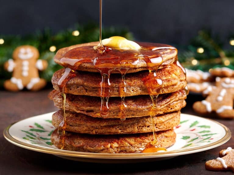 Side view of a stack of gingerbread pancakes with butter and syrup being drizzled over.