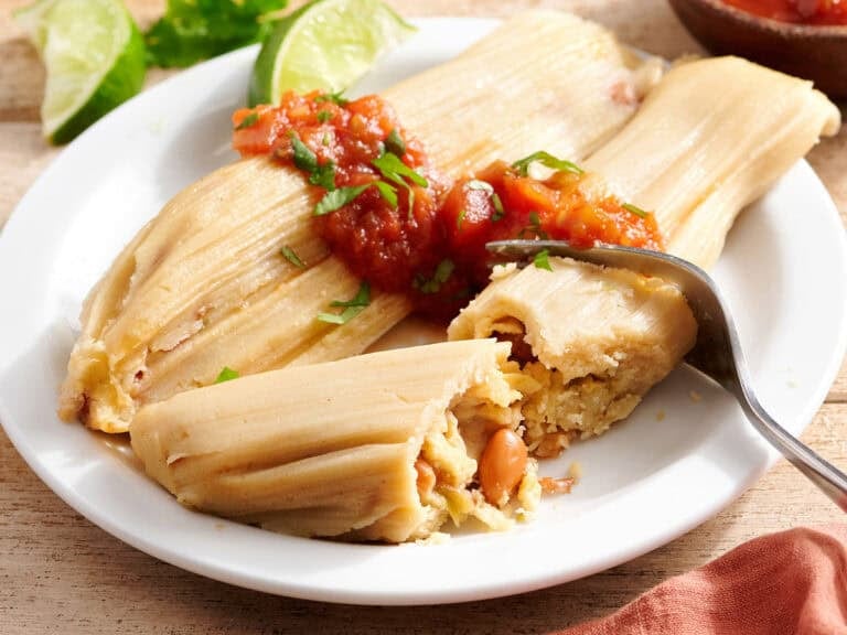 Side view of bean tamales on a plate with salsa.
