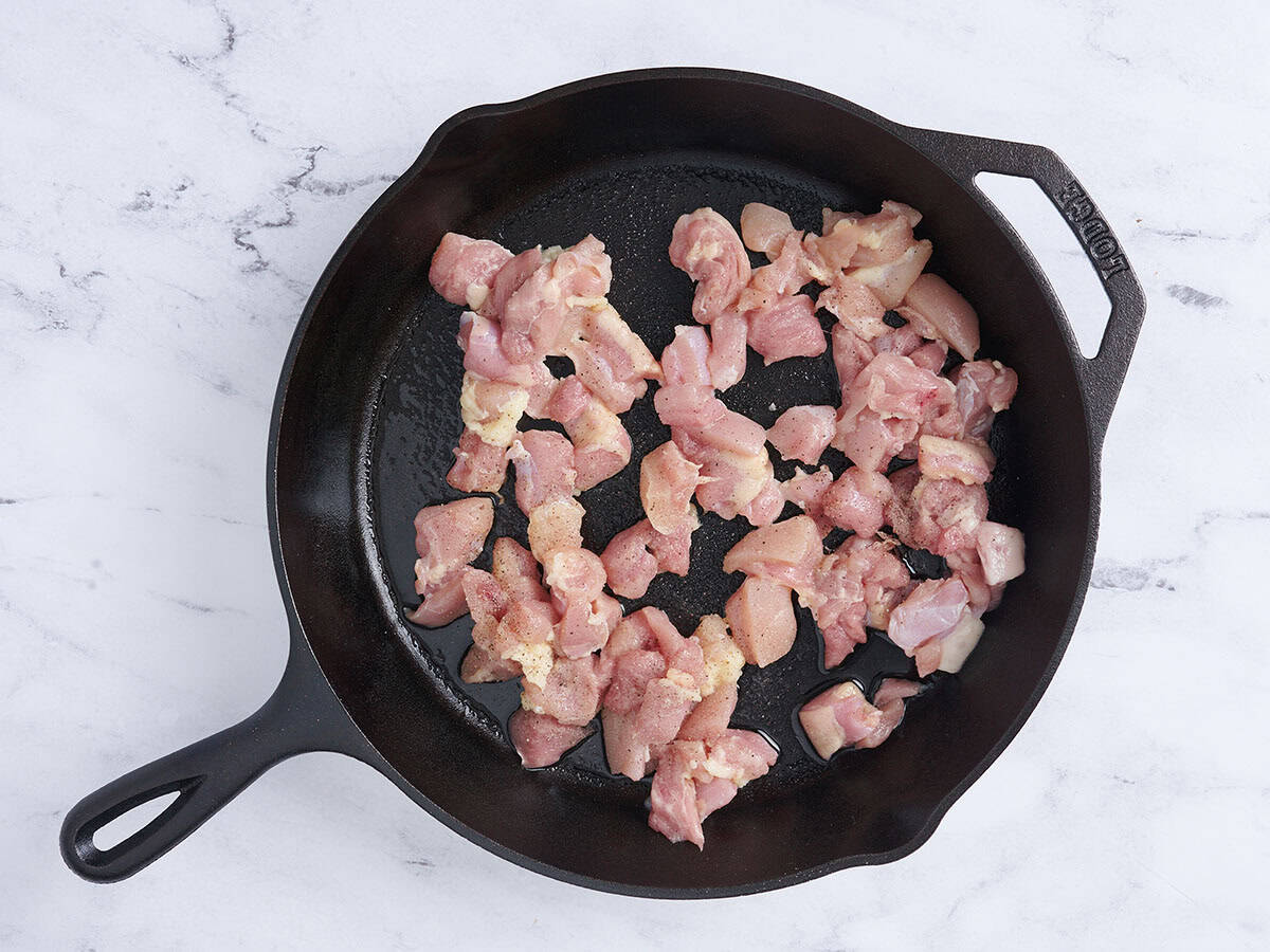 Chicken thigh pieces cooking in a skillet.