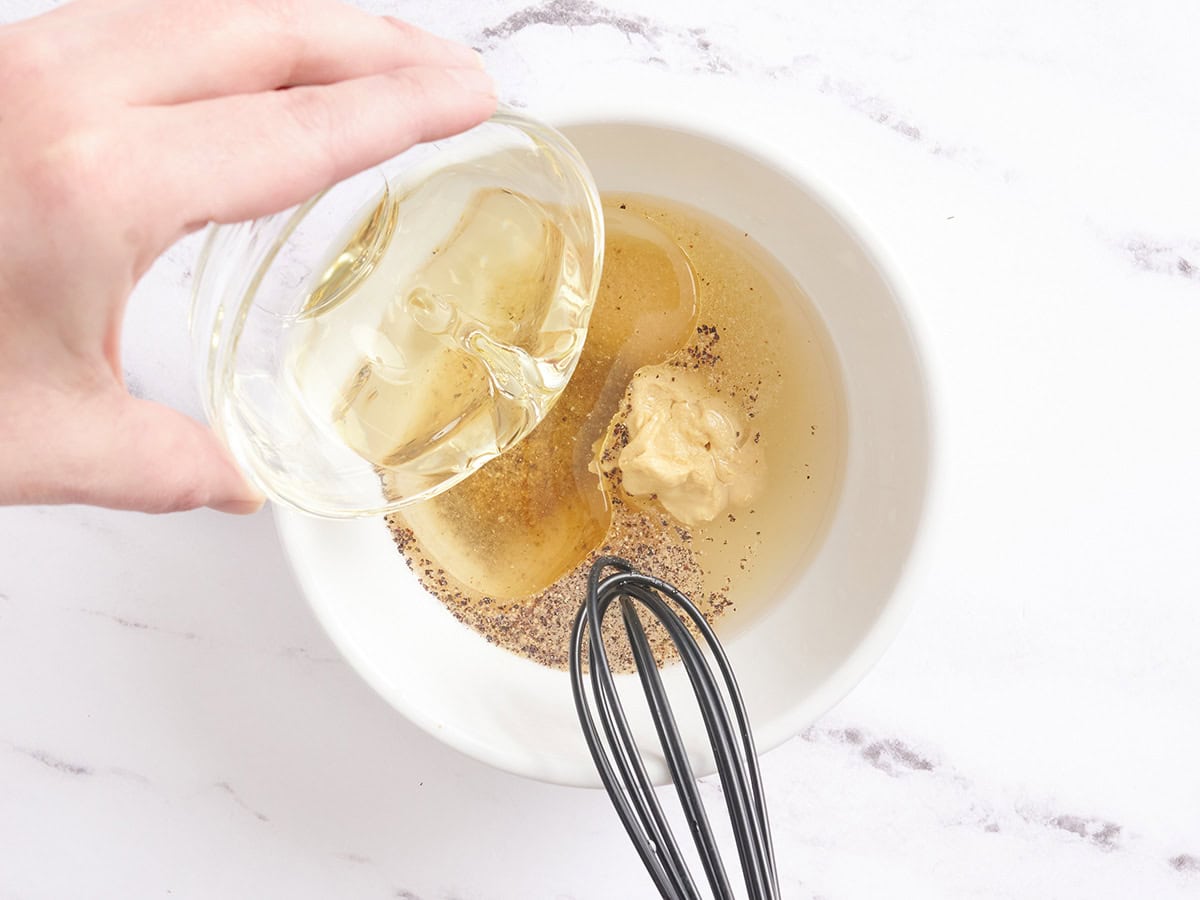 Oil being streamed into a bowl to make a vinaigrette.