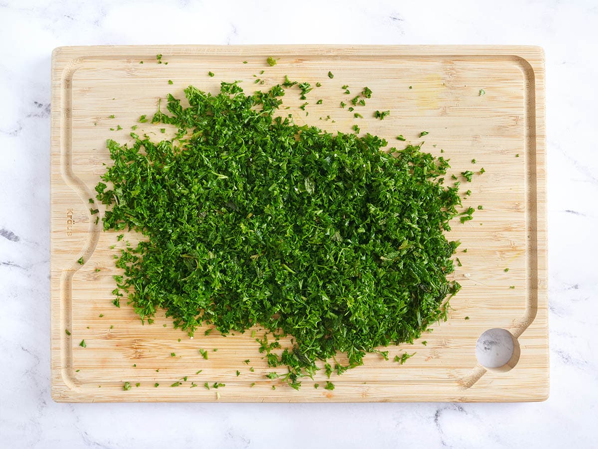 Minced parsley and mint on a chopping board.
