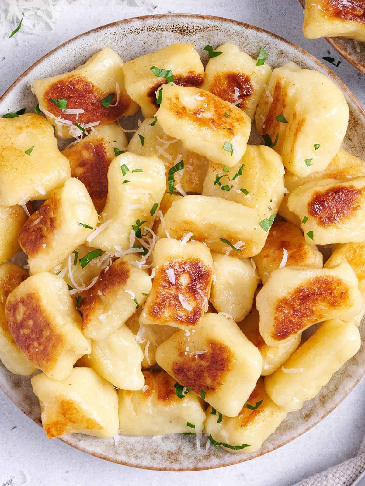 Plate of pan fried potato gnocchi garnished with parsley and Parmesan.
