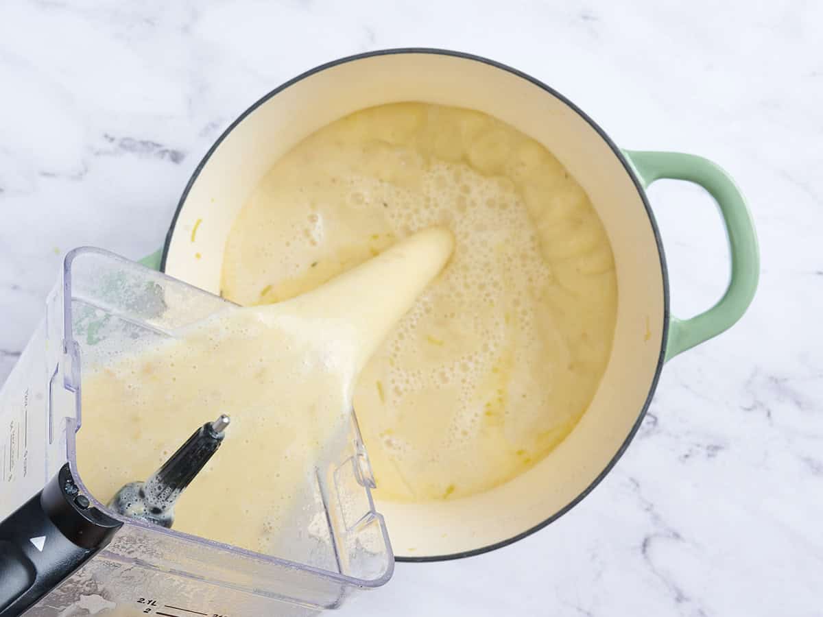 Blended potato leek soup being poured into a larger pot.