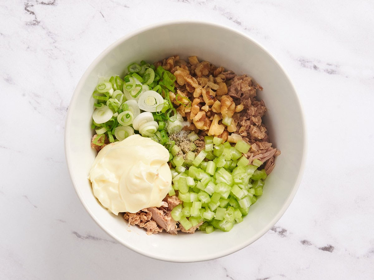 Diced celery, green onions, canned tuna, walnuts, seasonings and mayo in a bowl.