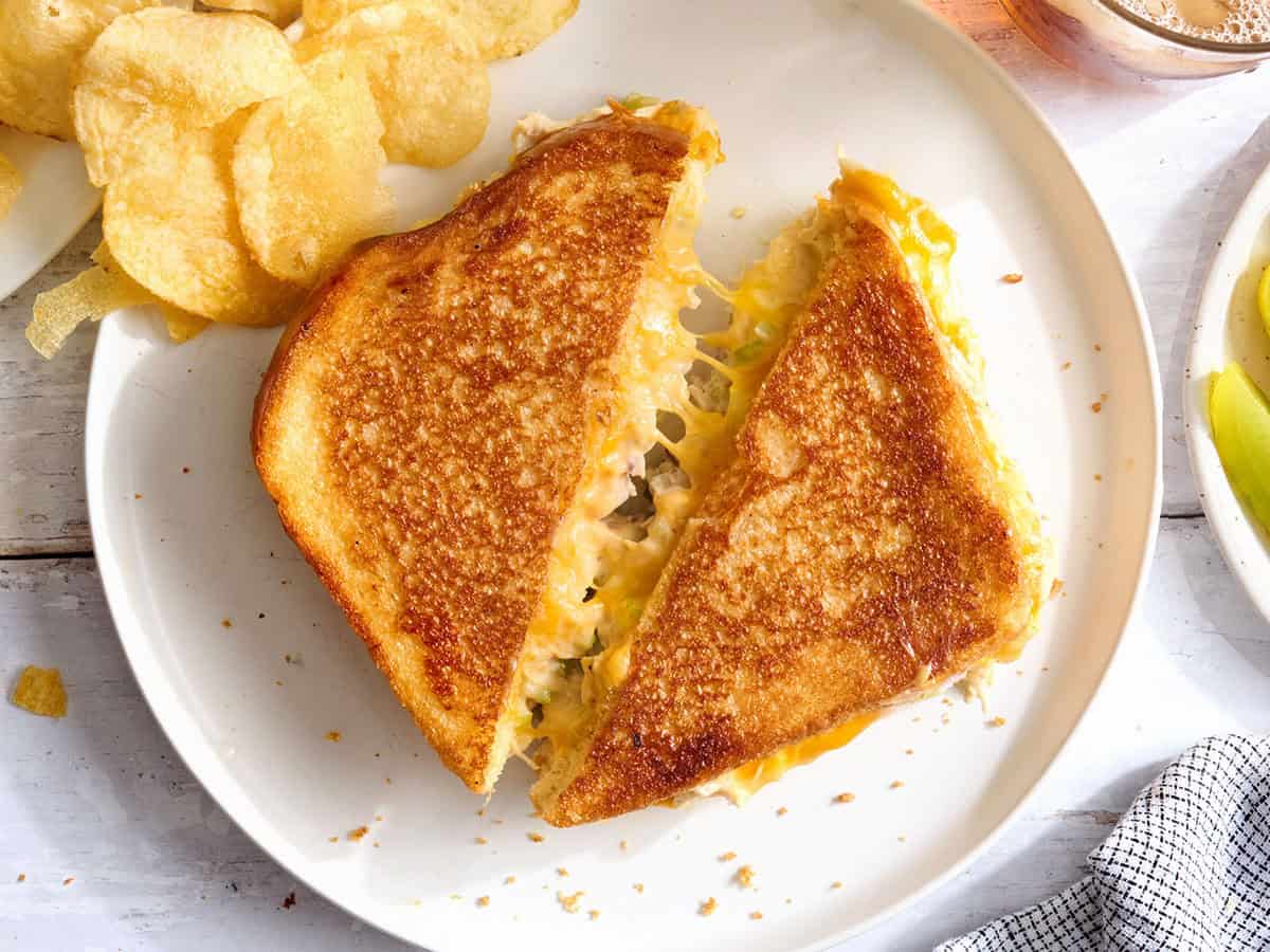 Classic tuna melt sandwich cut in half on a white plate with chips. 