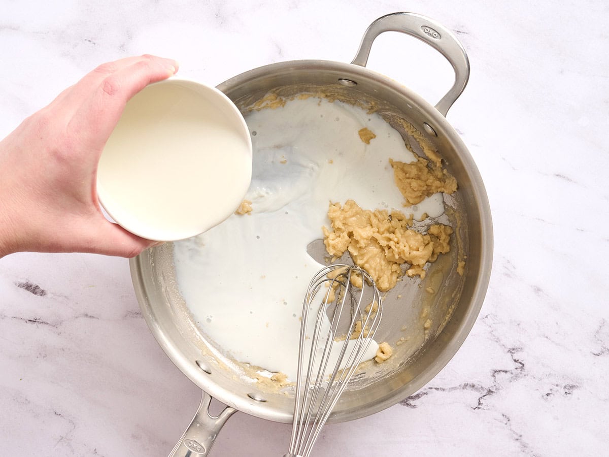 Milk being whisked into a roux in a skillet.