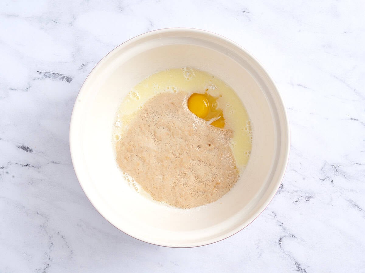 Adding milk, yeast, and eggs to the flour and sugar.